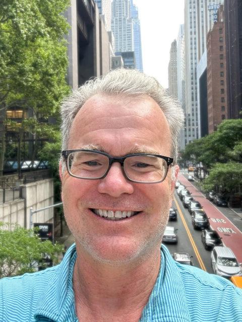 Picture of man wearing glasses with city in the background.